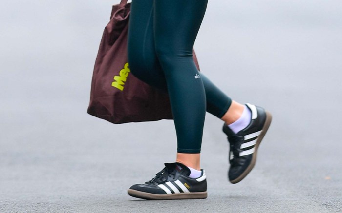 woman wearing black adidas leather walking shoes, blue leggings, and carrying a red tote bag