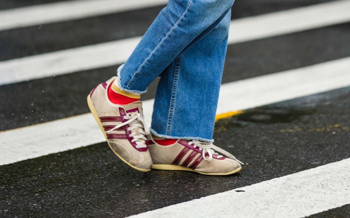 person wears jeans and burgundy striped Adidas sneakers