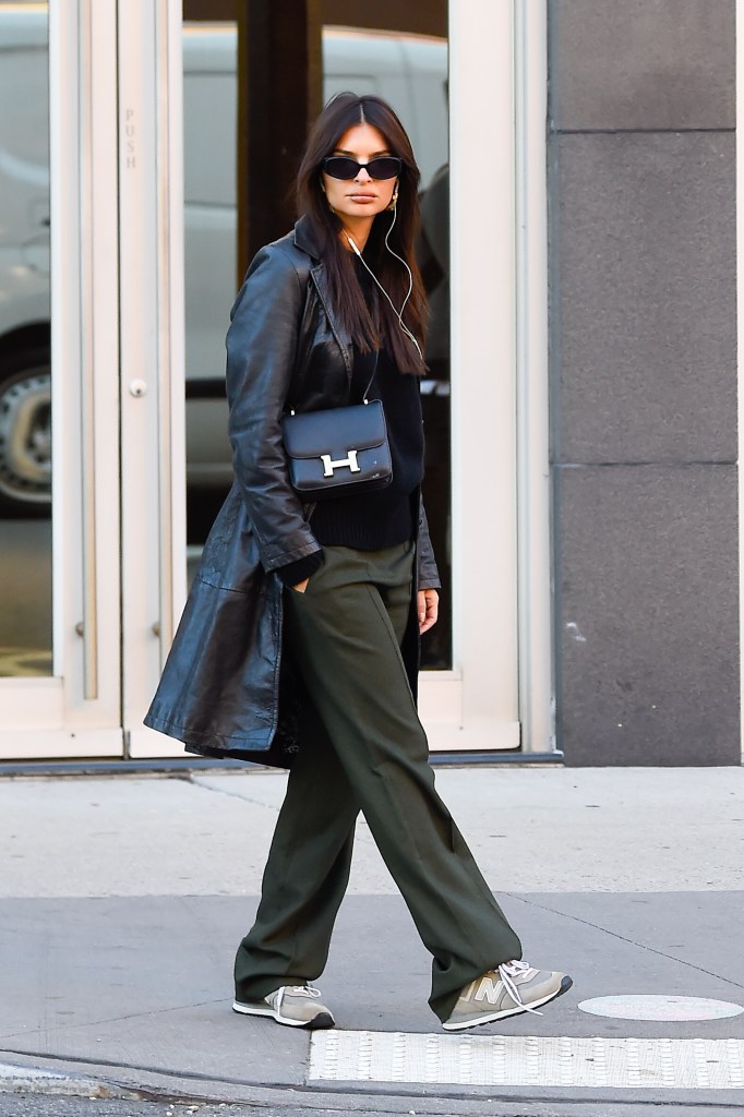 Emily Ratajkowski is seen wearing gray New Balance 574 sneakers with green pants, a leather jacket, and crossbody bag